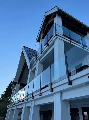 White house with glass balconies, black railing, blue sky.