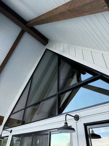 Triangular window with black frame in a white-painted gable.  Wooden beams are visible. 