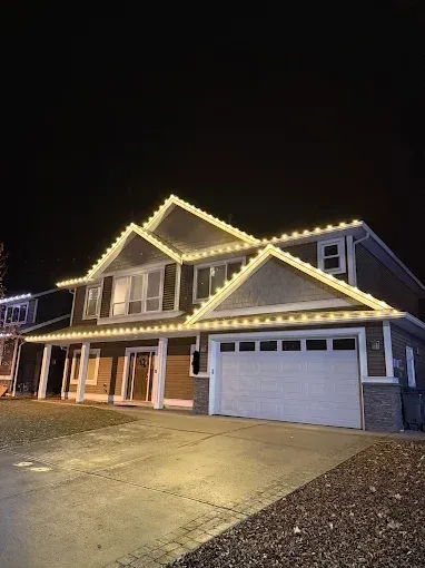 A two-story house at night, illuminated with white Christmas lights along the rooflines.