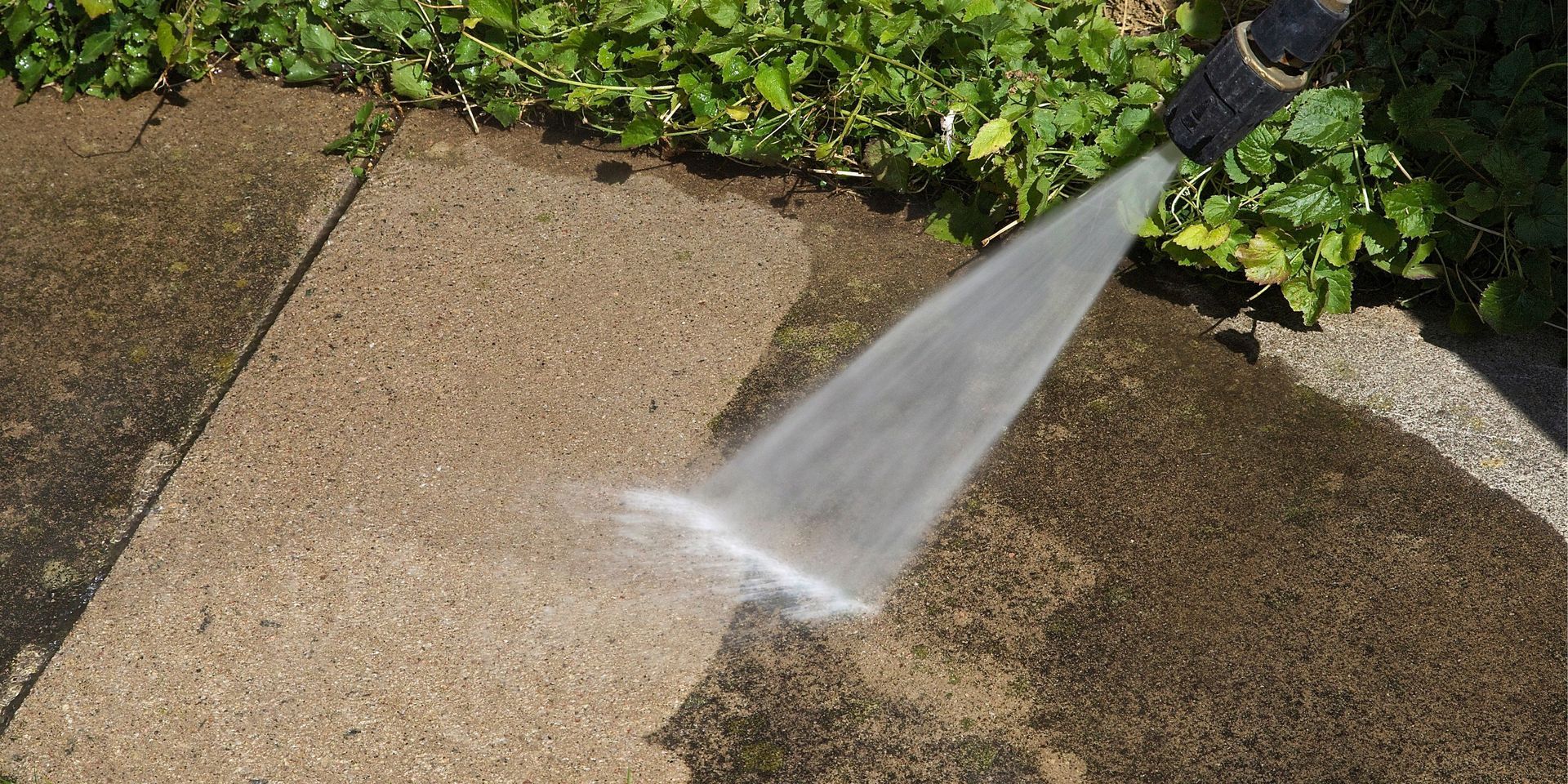 Pressure washing a concrete surface. Water sprays from the hose, cleaning the dirty area.
