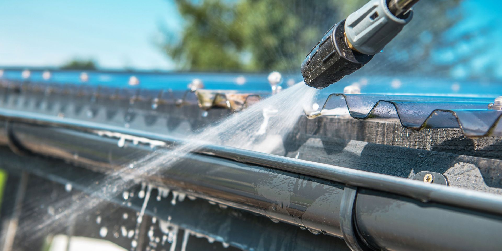A gutter is cleaned with a pressure washer, spraying water.