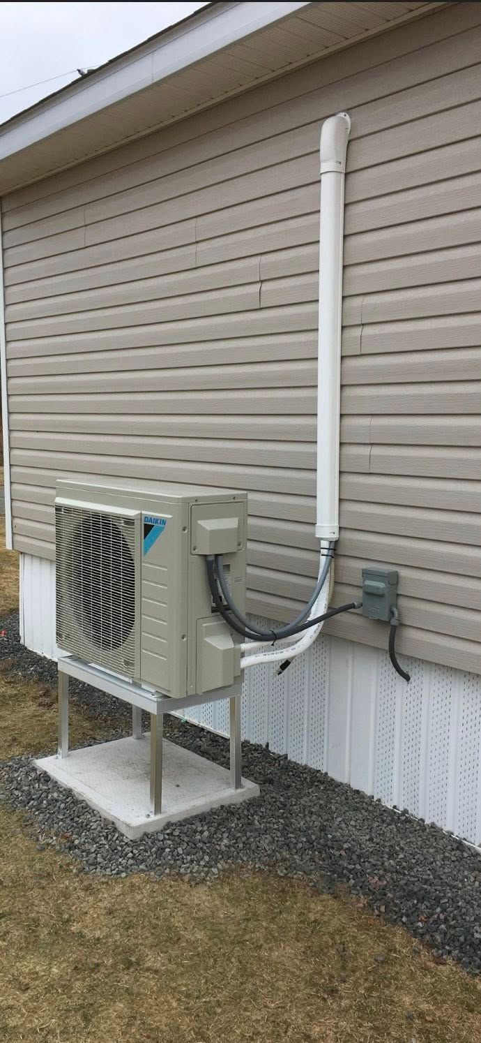 An air conditioning unit is installed on a concrete pad next to a house with light siding.