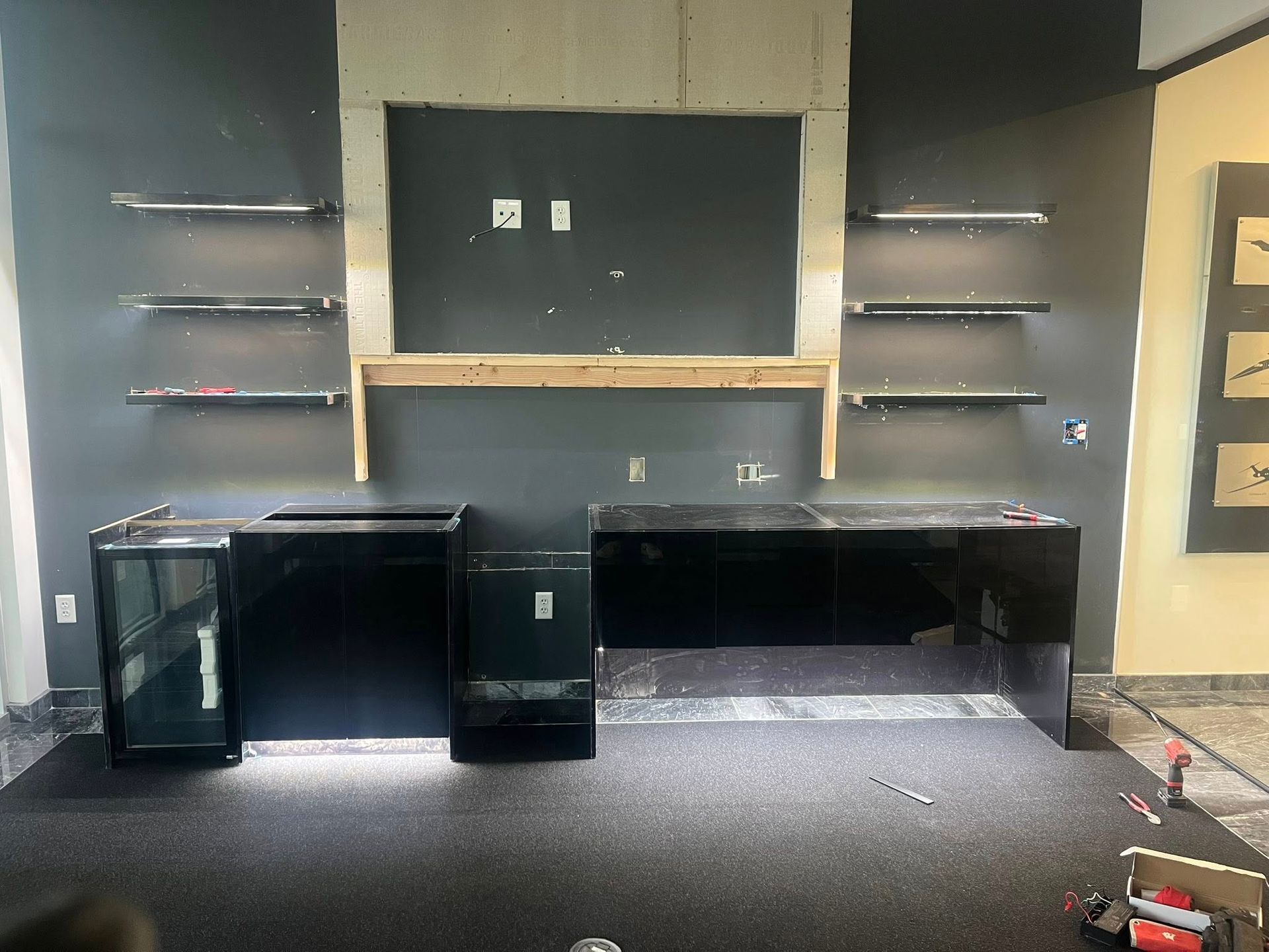Office setup with black desks and shelves on a gray wall. A monitor area is framed in wood.