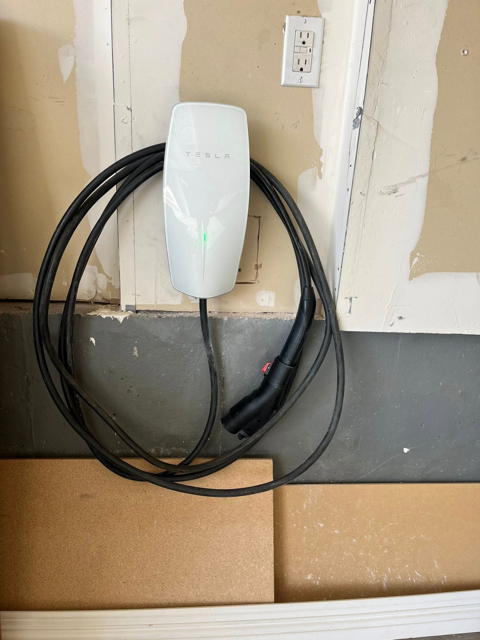 White Tesla charger mounted on a wall in a garage, cable coiled below.