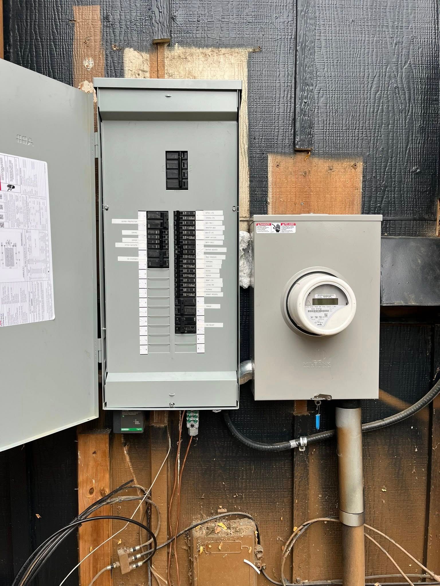 Electrical panel and meter box mounted on a weathered wooden exterior wall.