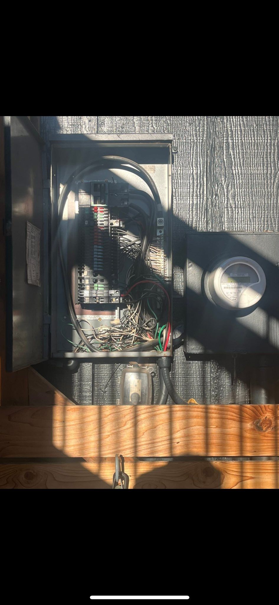 Electrical panel with meters and circuit breakers. Sunlight casts shadows on wooden surface.