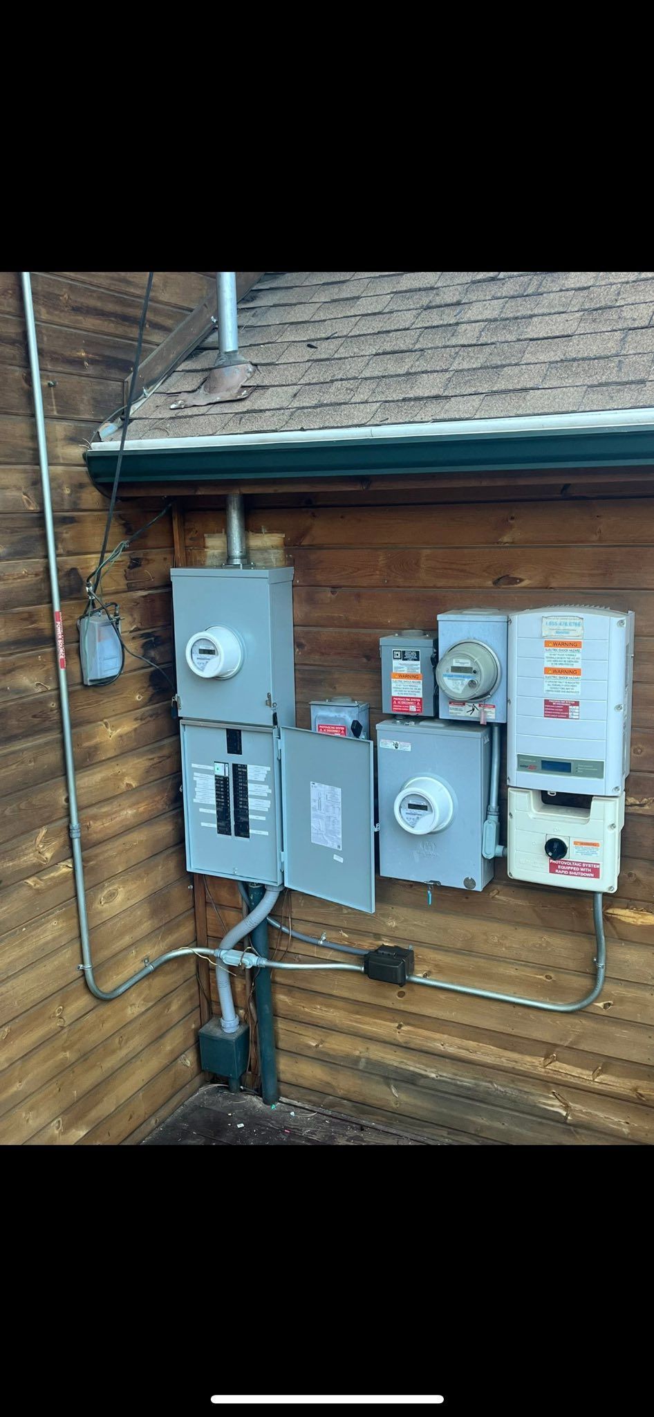 Electrical panel boxes mounted on a wooden building, with various components and conduit.