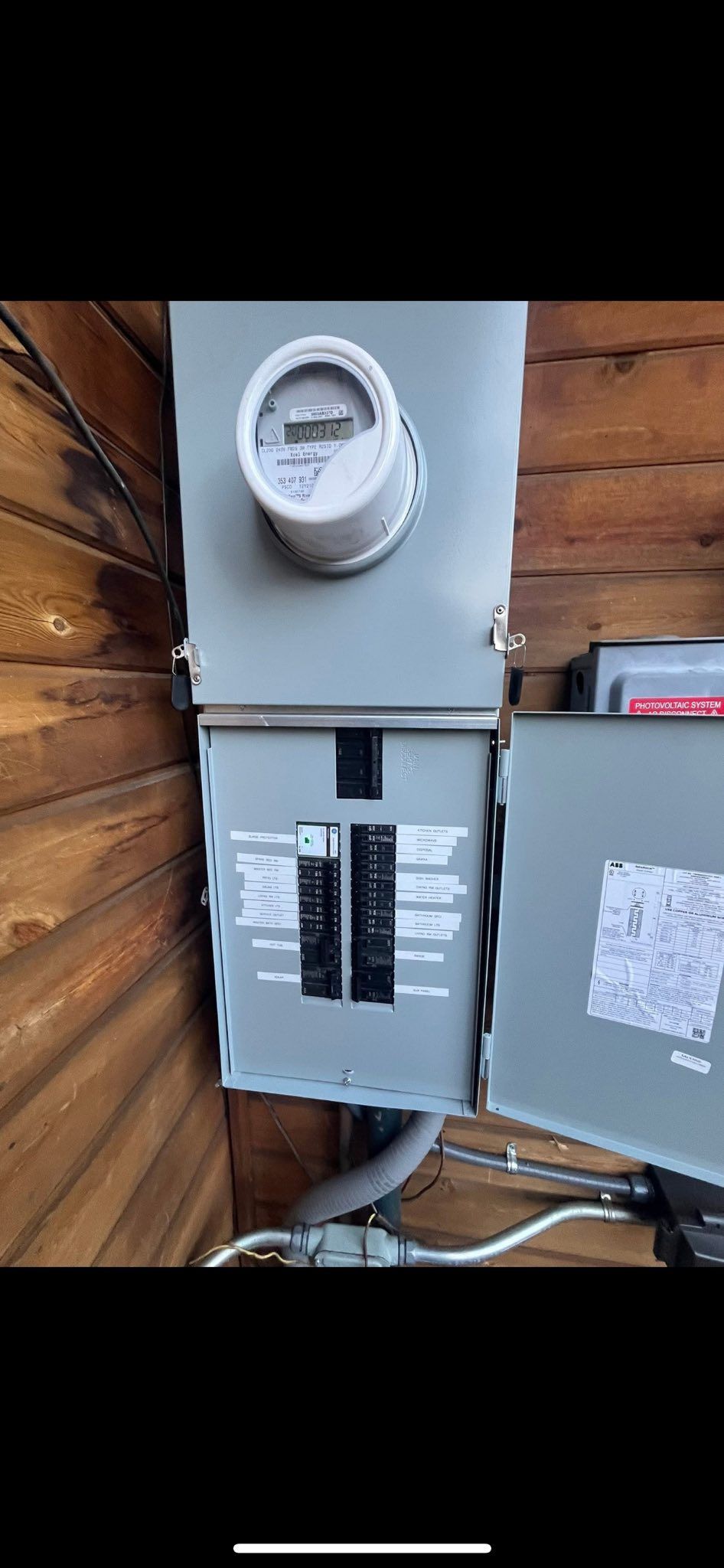 Electric meter box mounted on a wood wall. Contains a meter, circuit breakers, and wiring.