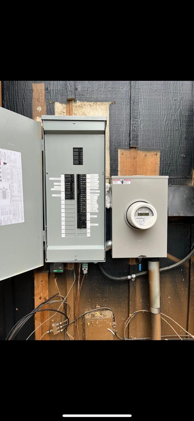 Electrical panel with circuit breakers, meter box, and wiring mounted on a wooden wall.