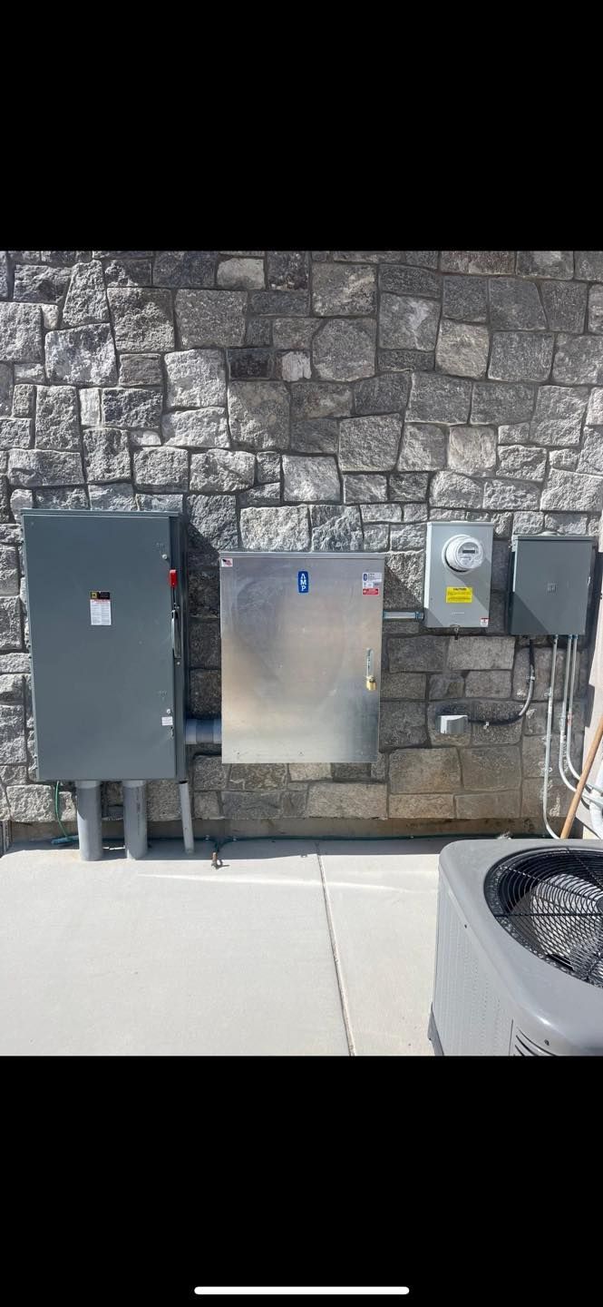Electrical boxes mounted on a stone wall, including a meter and a large gray box with conduit.