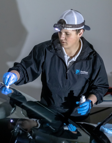 Mechanic in gloves and headlamp inspecting a car windshield in a garage