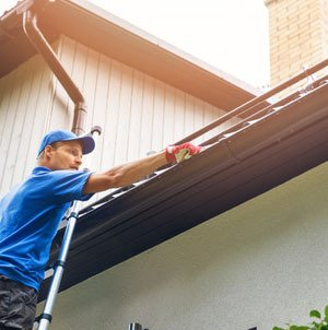 Man on ladder cleaning house gutter from leaves and dirt