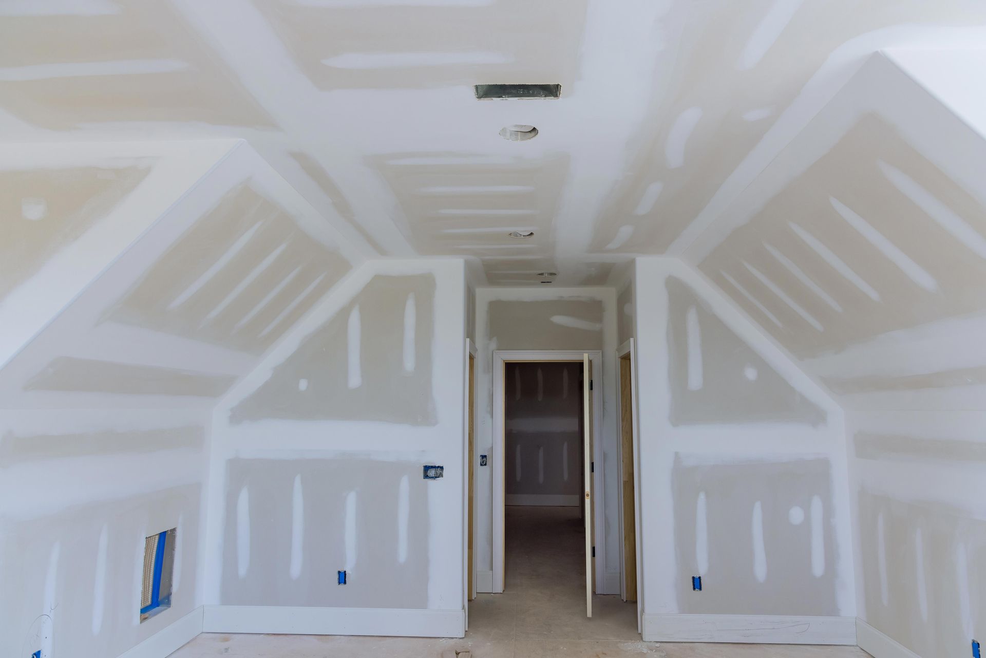 Unfinished drywall room with white taped seams, sloped ceiling, and open doorway. Unfinished drywall room with white taped seams, sloped ceiling, and open doorway.