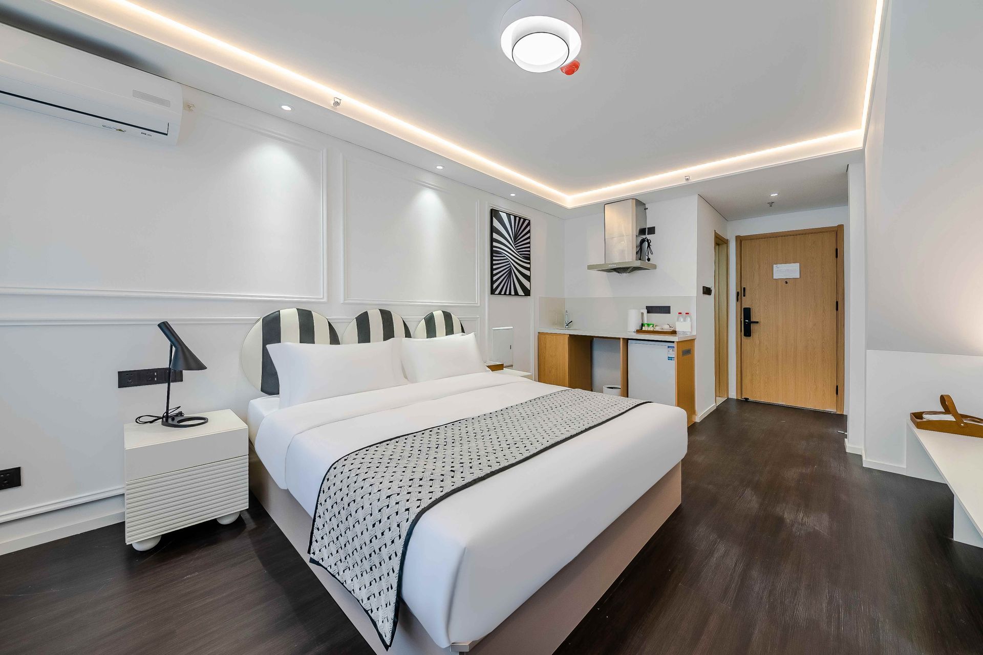 Modern bedroom with white bedding, dark wood floors, desk, and kitchenette area Modern bedroom with white bedding, dark wood floors, desk, and kitchenette area