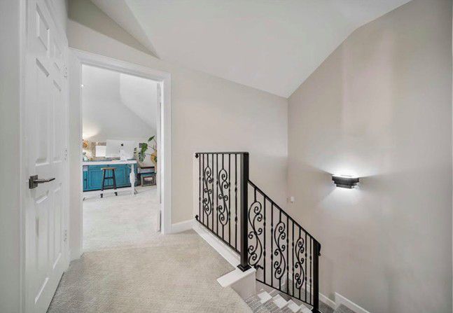 Bright upstairs hallway with white walls, carpet, stair railing, and a view into a blue-accented room Bright upstairs hallway with white walls, carpet, stair railing, and a view into a blue-accented room