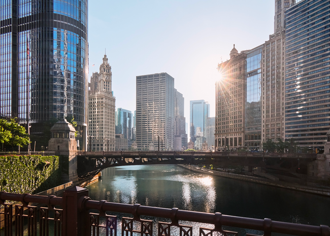 The sun is shining through the windows of a bridge over a river in a city.