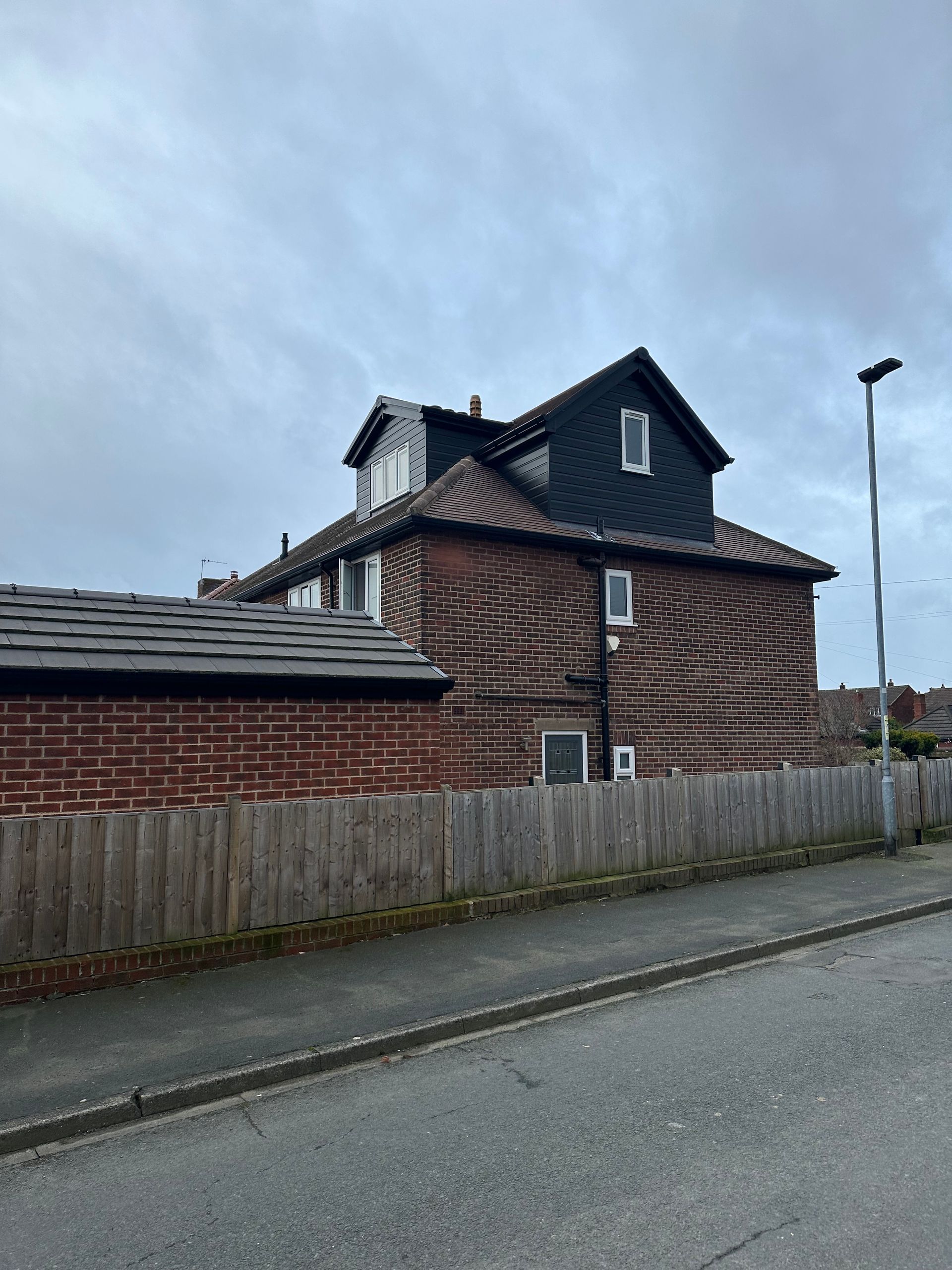 A large brick house with a black roof is behind a wooden fence.