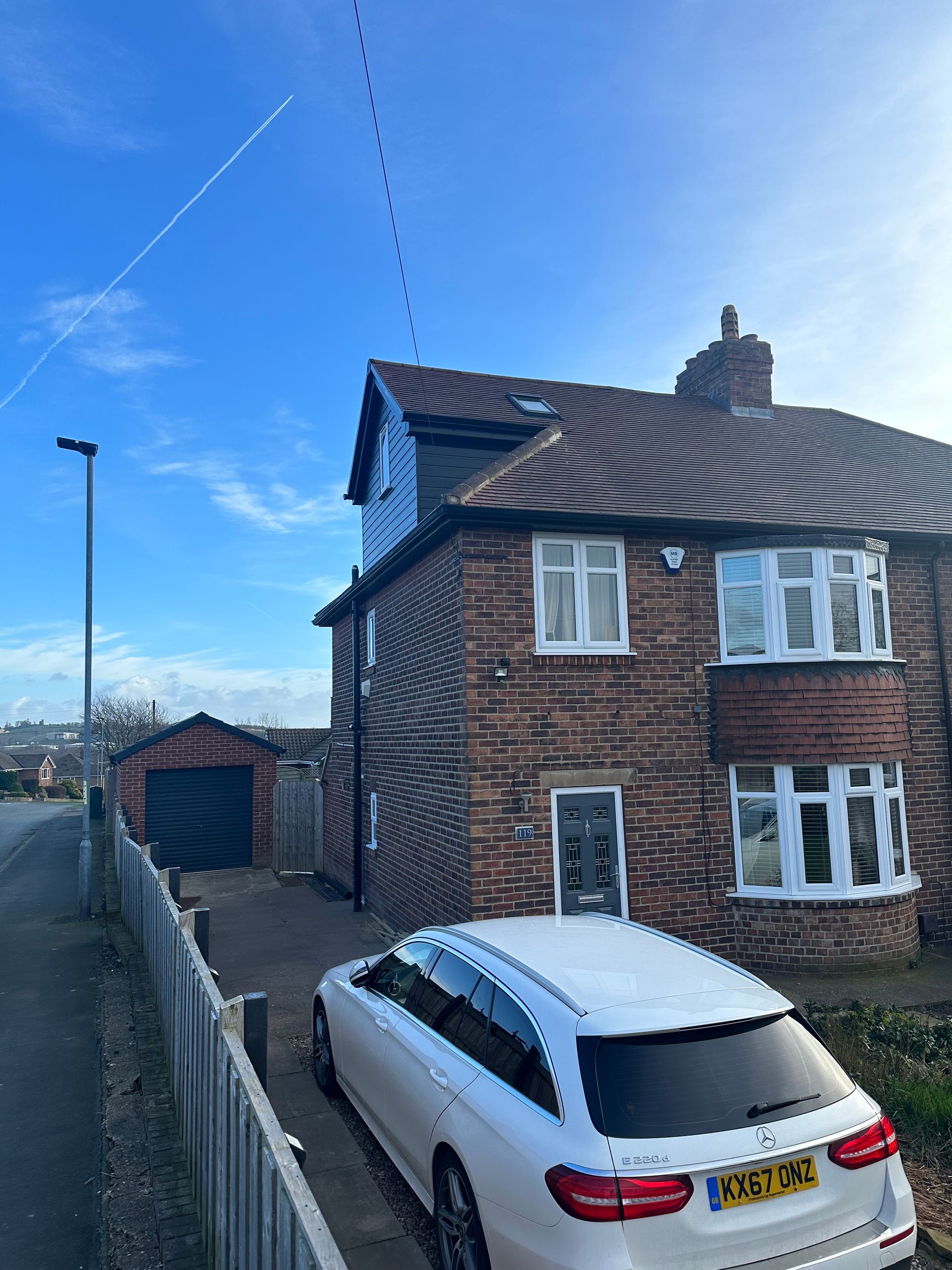 A white car is parked in front of a brick house.