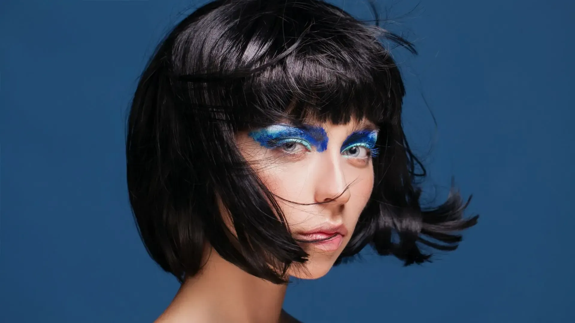 A woman wearing a wig and blue makeup is looking at the camera.