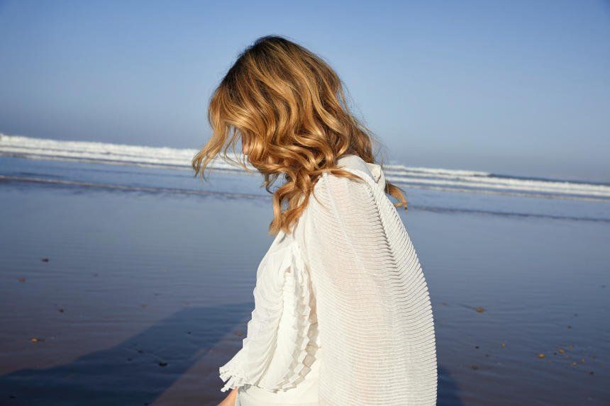 a woman in a white dress is standing on a beach looking at the ocean .