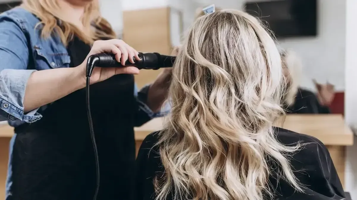 Blonde woman getting her hair styled at a salon. Stylist uses a hair dryer.