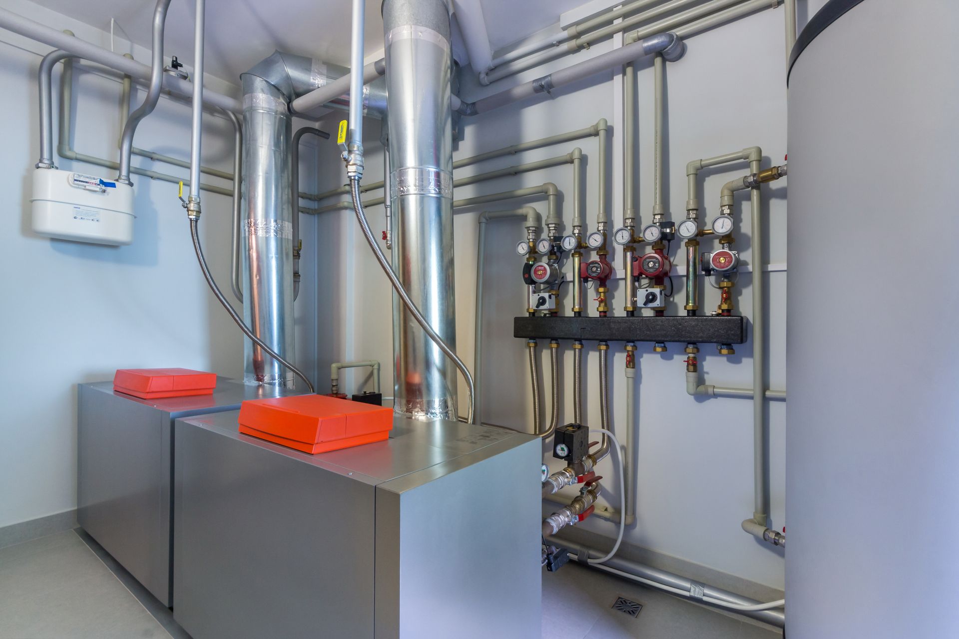 Une buanderie avec équipement de chauffage : deux boîtes argentées, des tuyaux et un chauffe-eau.