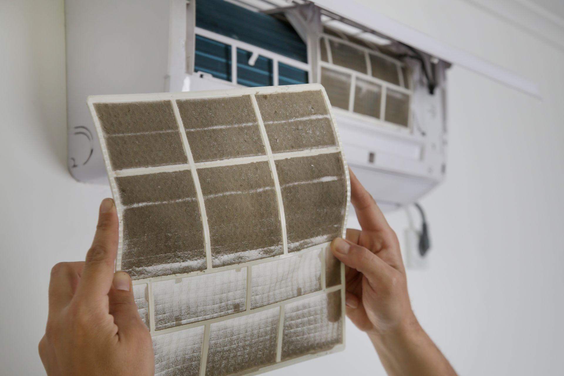 Personne tenant un filtre de climatisation très sale devant l'appareil.