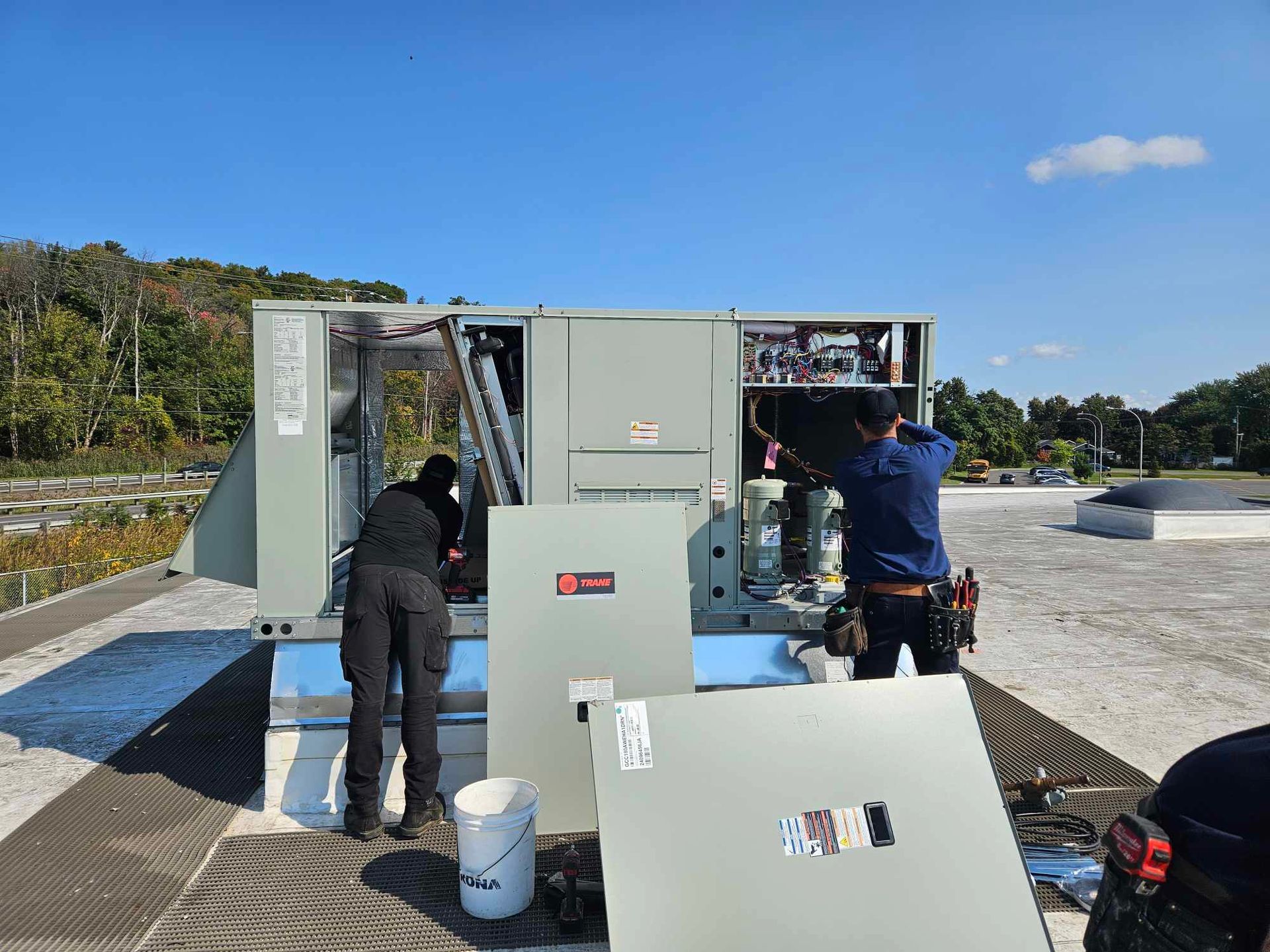 Deux techniciens CVC travaillant sur une unité de climatisation sur le toit par une journée ensoleillée.