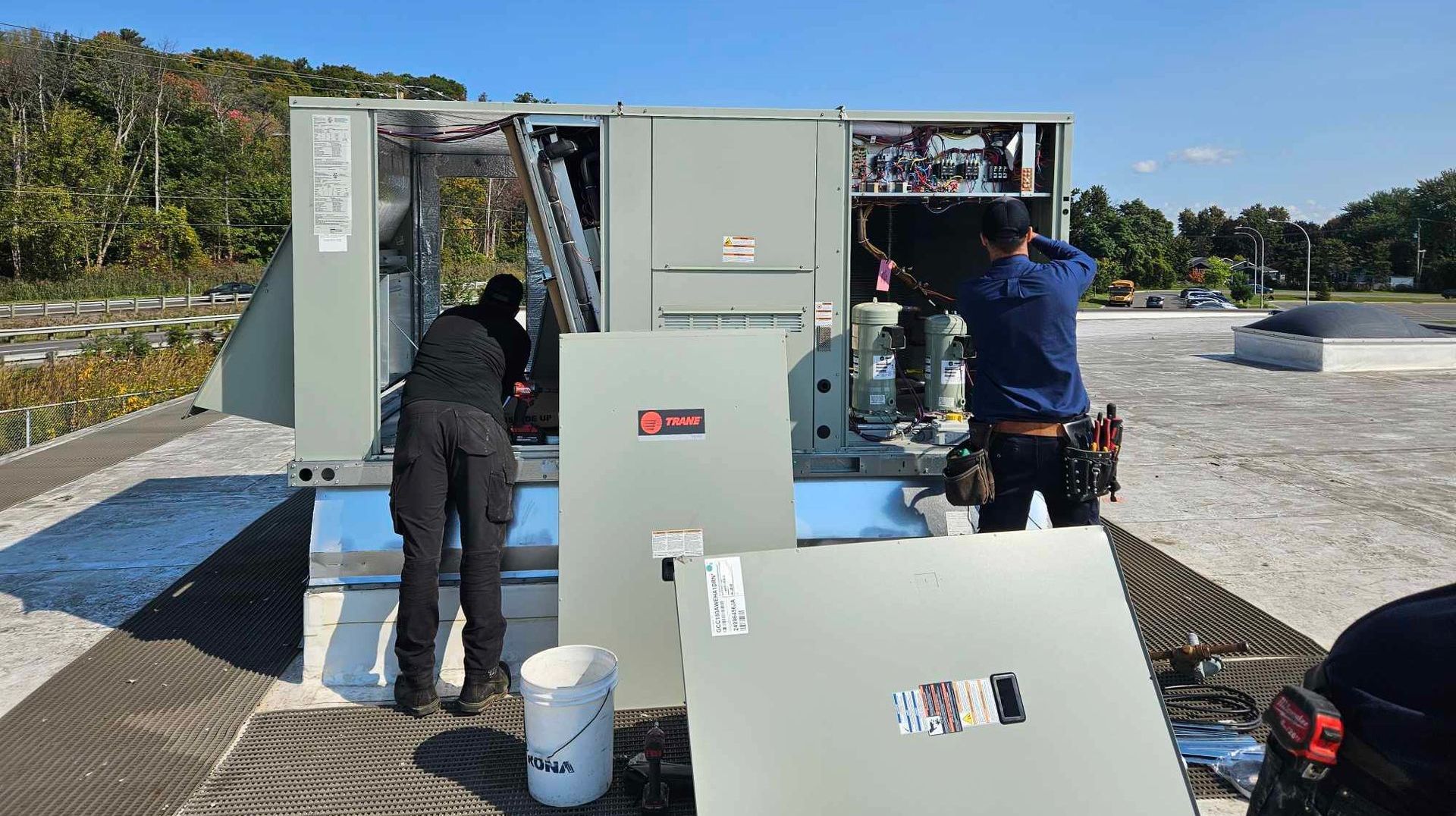 Two men are working on an air conditioner on top of a truck.