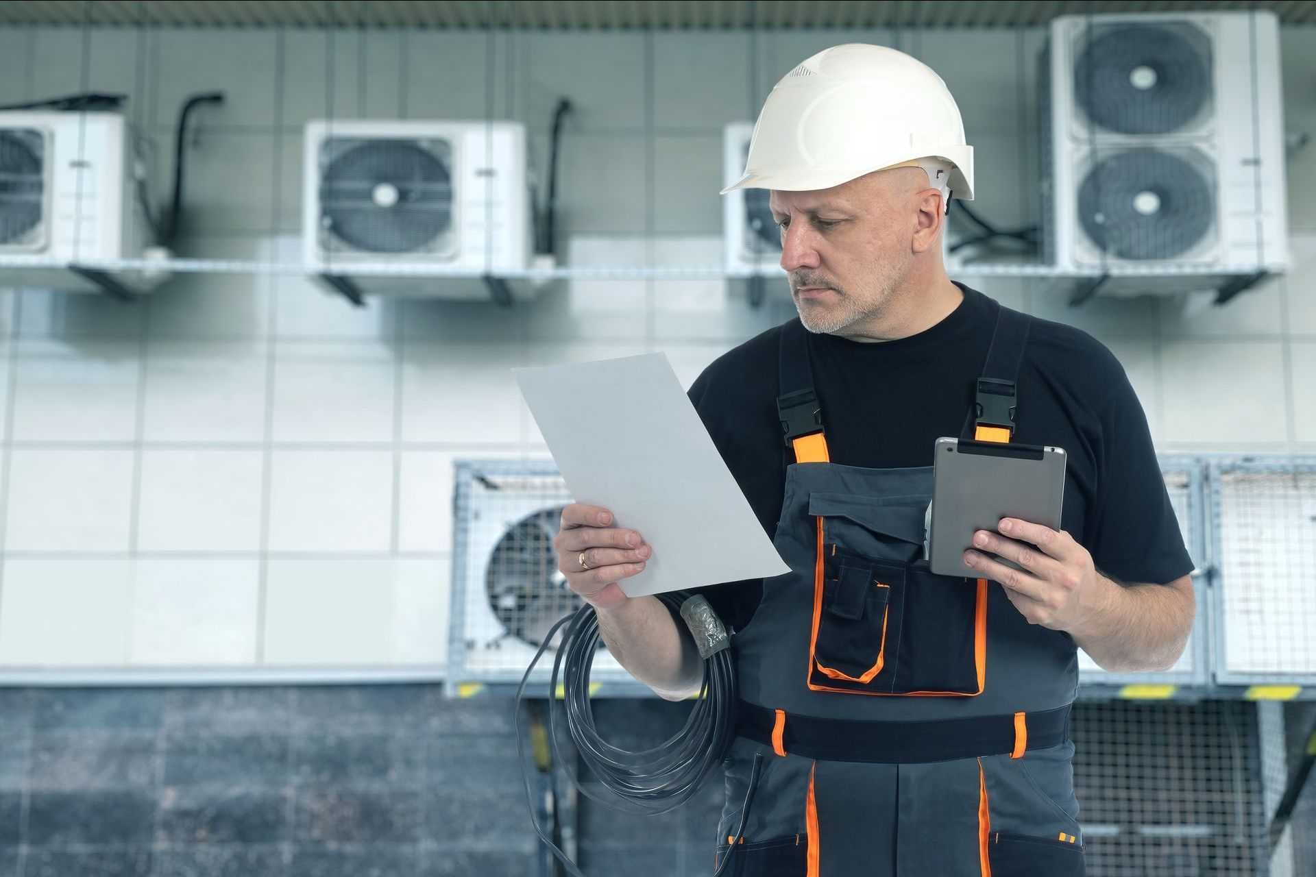 Un homme portant un casque tient une tablette et regarde un morceau de papier.