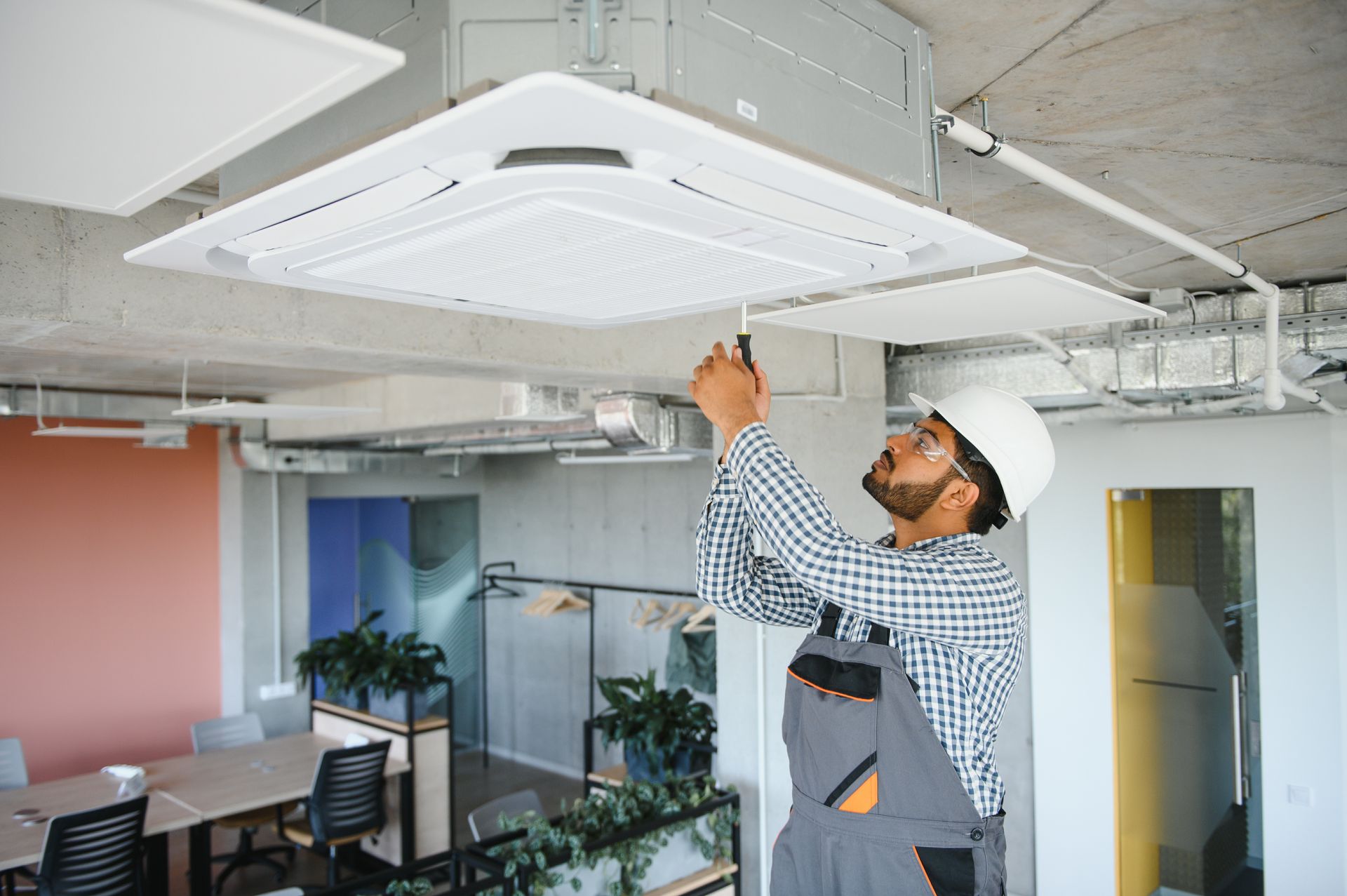 Un homme travaille sur un climatiseur dans un bureau.