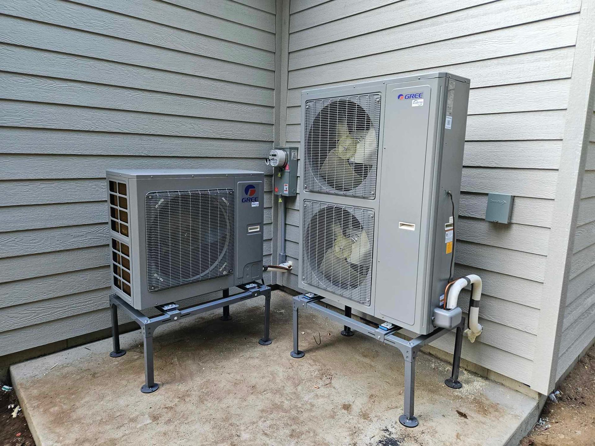 Deux unités de climatisation grises sur des supports métalliques, contre le revêtement d'un bâtiment.