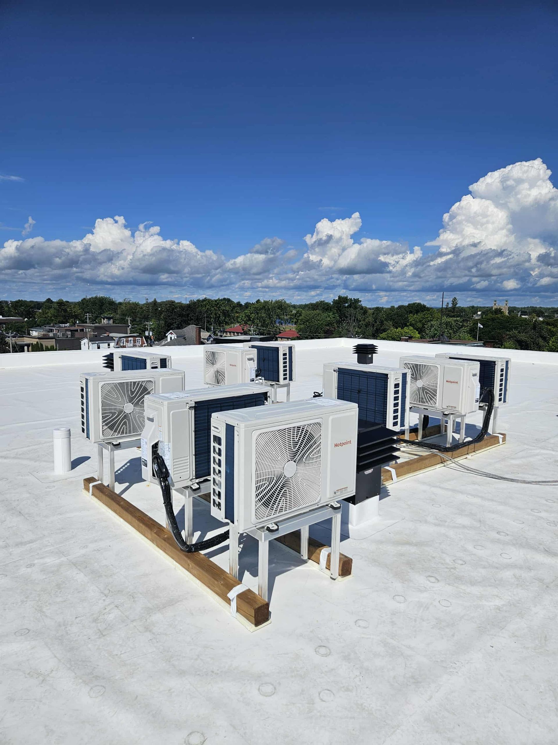 Unités CVC sur un toit blanc, sous un ciel bleu avec des nuages.