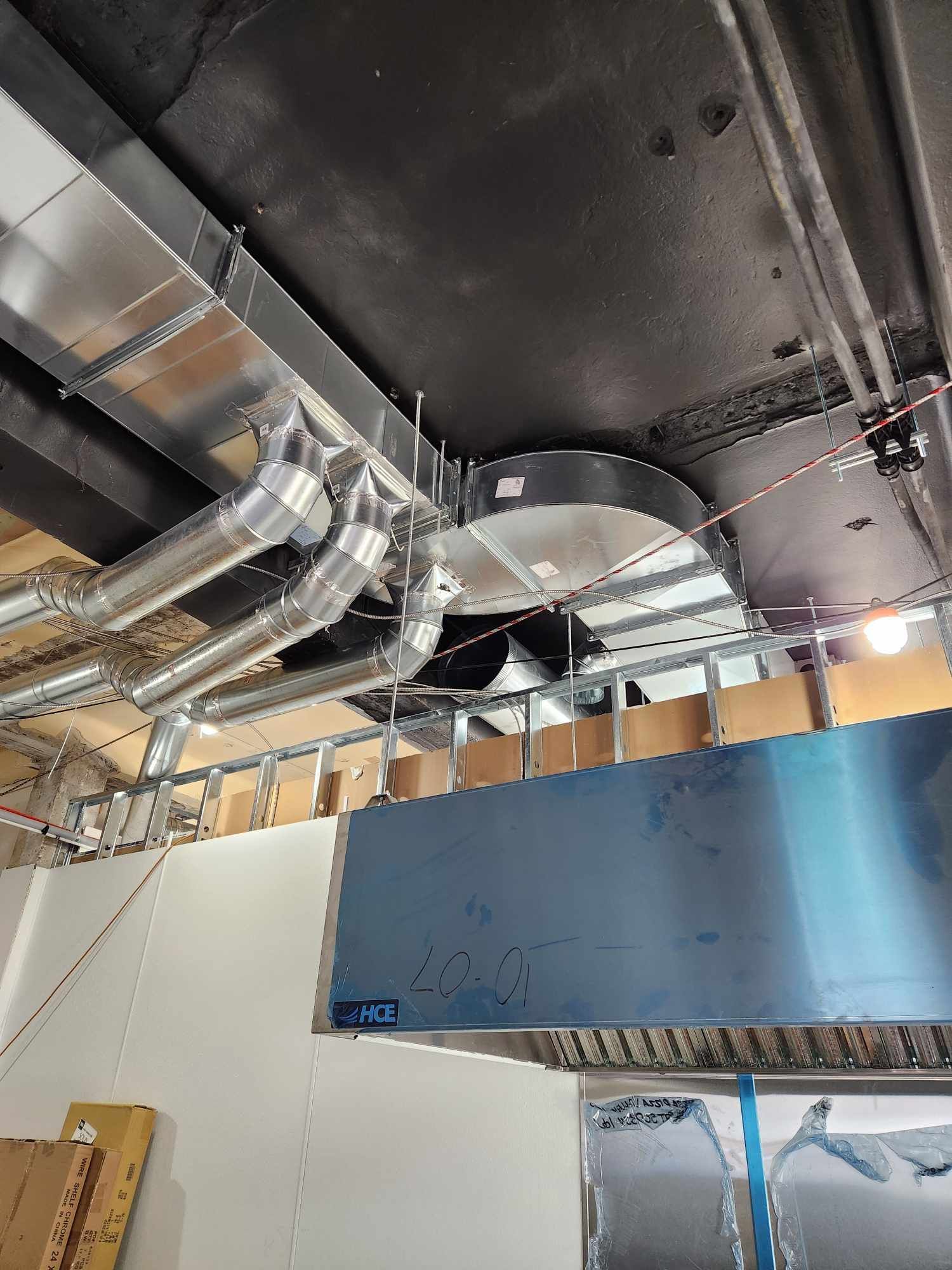 Conduits de ventilation métalliques et hotte installés dans le plafond d'une cuisine commerciale.