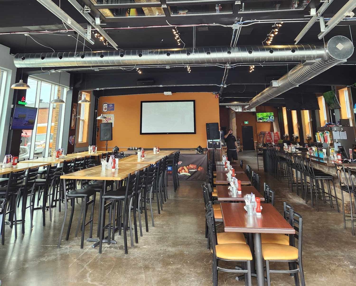 Une grande salle à manger avec tables et chaises et un écran de projection.