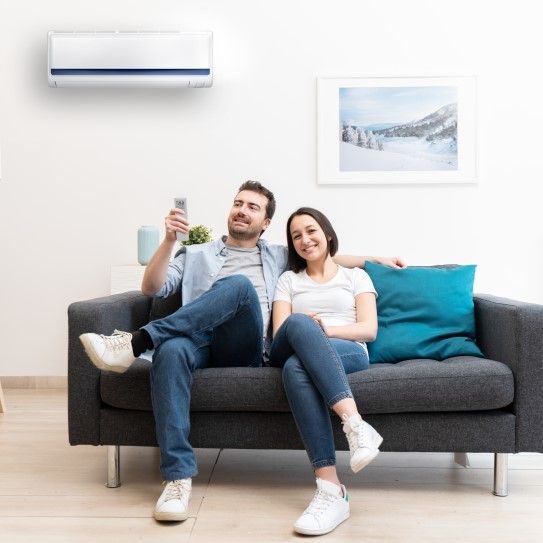 Couple sur un canapé avec télécommande, souriant, climatiseur au-dessus d'eux, peinture sur le mur.