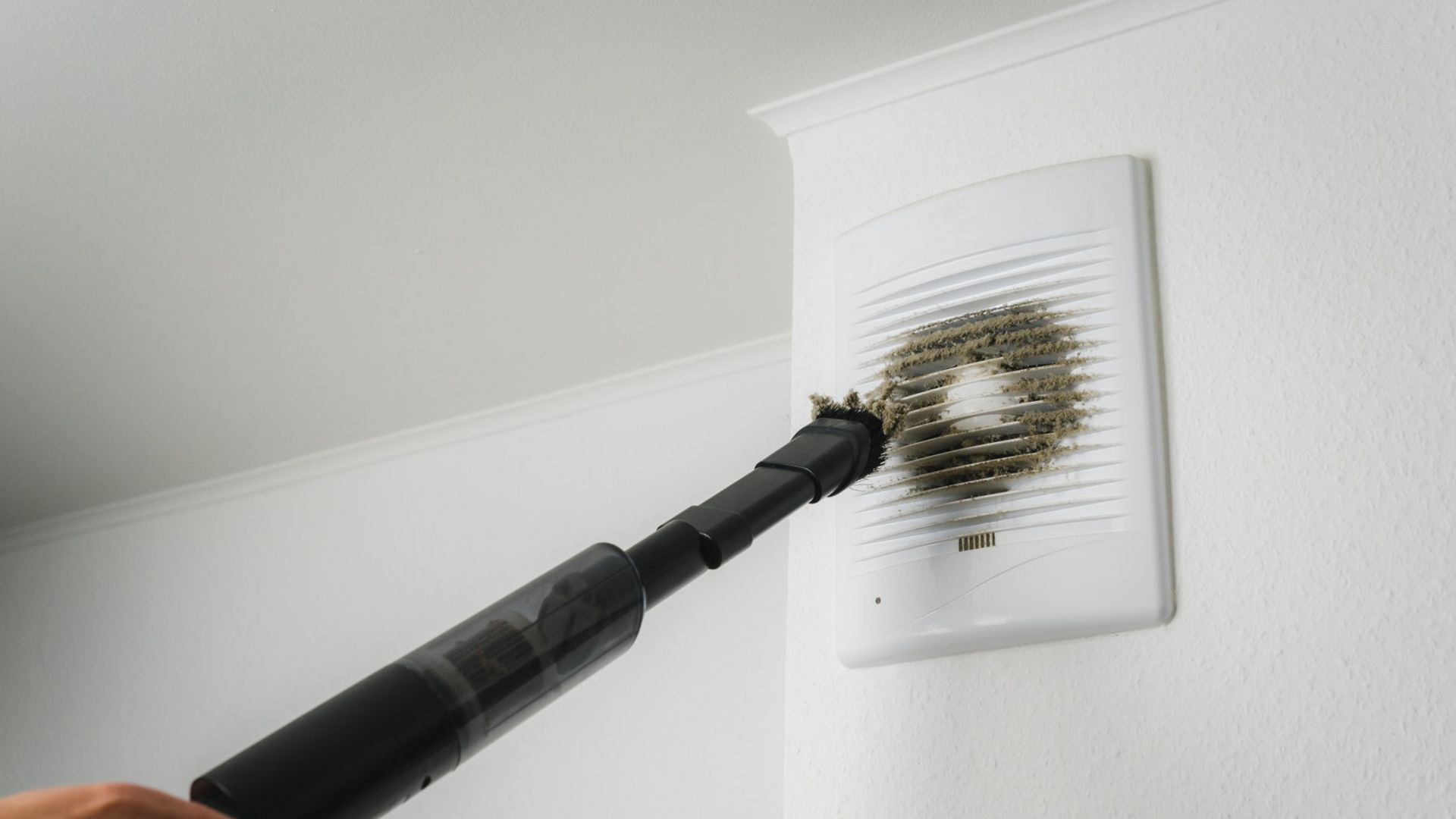 Une personne nettoie un ventilateur avec un aspirateur.