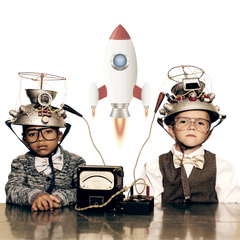 Two boys wearing strange hats are sitting at a table with a rocket in the background