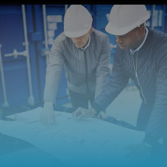 Two men wearing hard hats are looking at a blueprint.