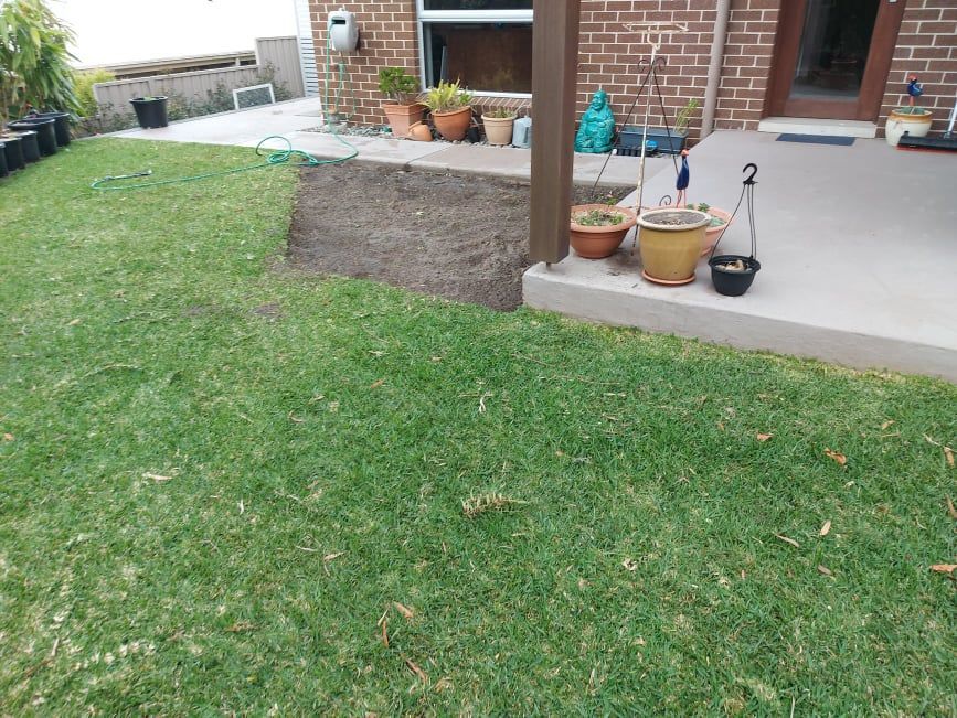 A Lawn With Potted Plants And A Brick House In The Background — Amaze Lawn and Garden Care In Nelson Bay, NSW