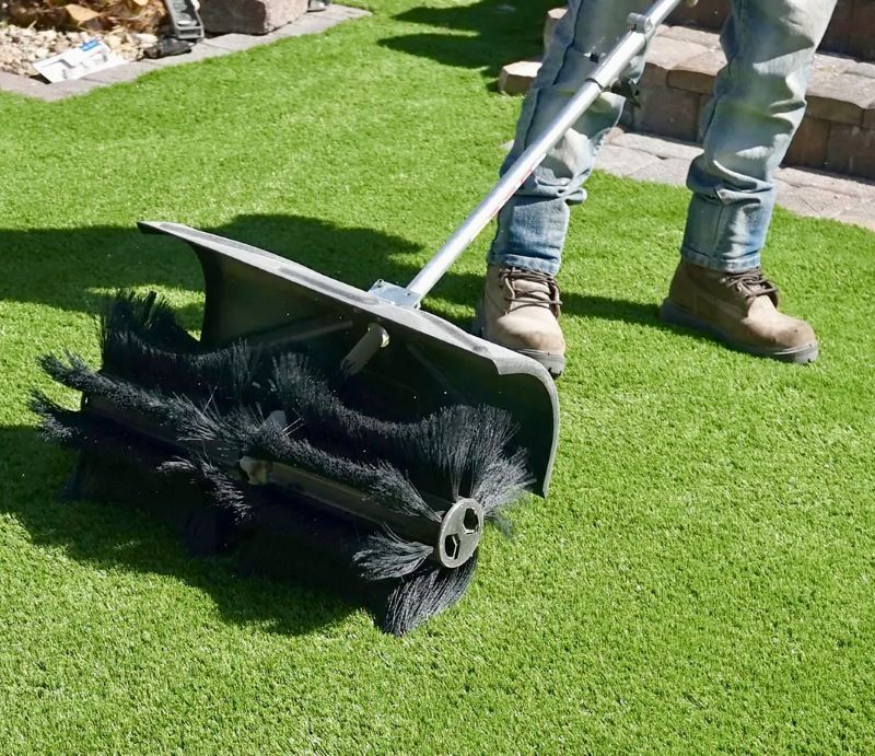 A Person Is Using A Broom On A Lush Green Lawn — Amaze Lawn and Garden Care In Nelson Bay, NSW
