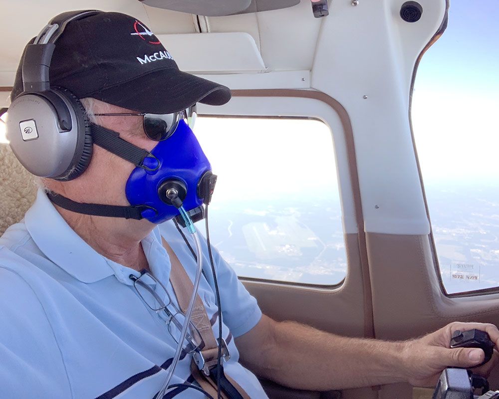 A pilot wearing a headset and blue oxygen mask while operating an airplane at high altitude.