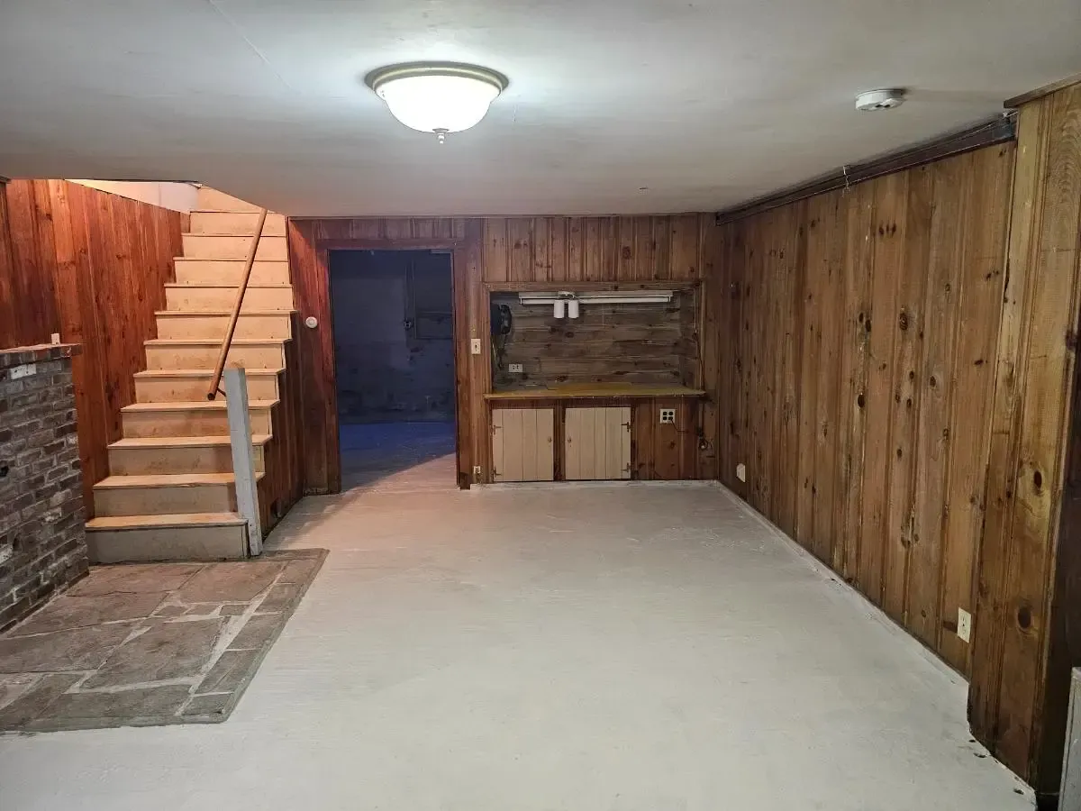 Basement room with wood paneling, stairs, and a built-in counter. Concrete floor. Dim lighting.