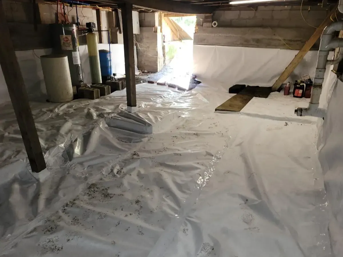 Basement with white plastic sheeting on floor and walls, supporting beams, various equipment, and an open doorway.
