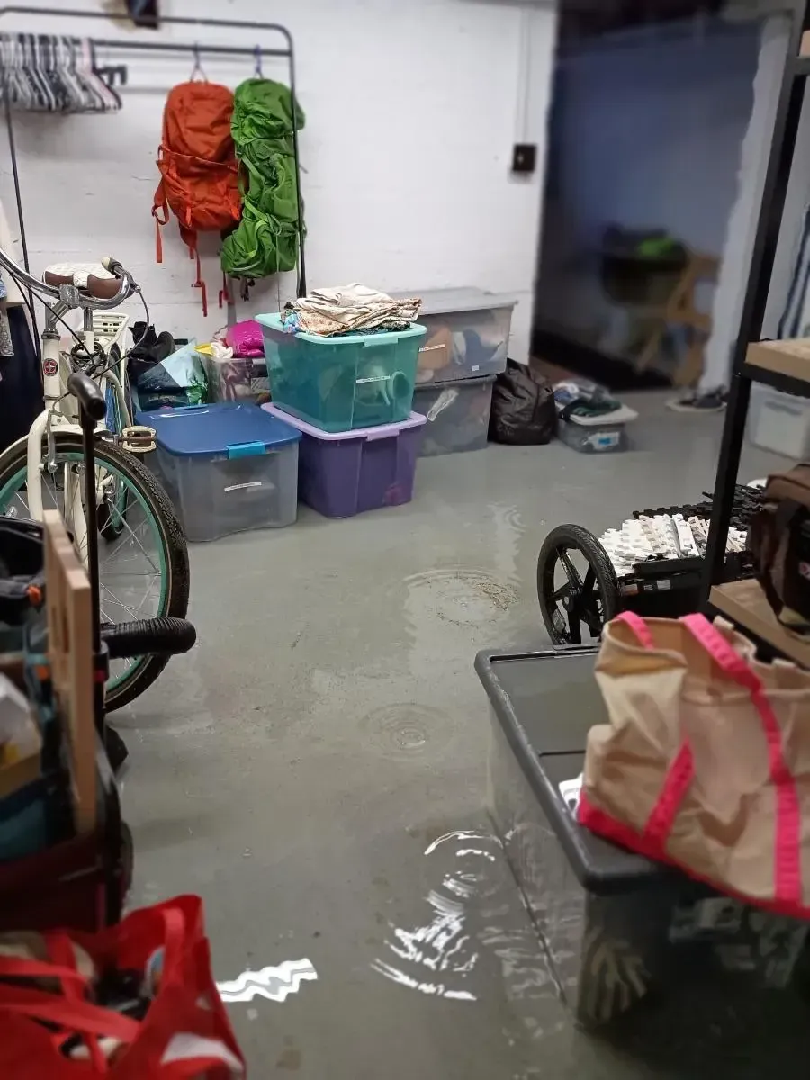 Flooded basement, water on concrete floor. Storage bins, backpack, and bicycle visible.