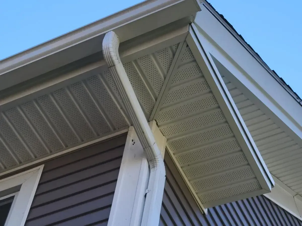 Beige gutters and soffit on a house with brown siding and a blue sky.