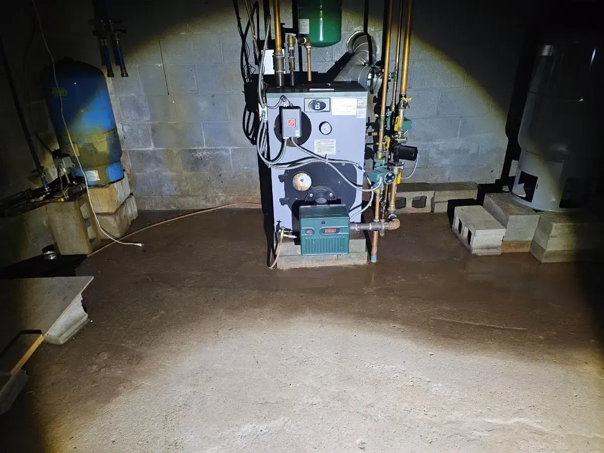 Dark basement with a furnace and water on the concrete floor.