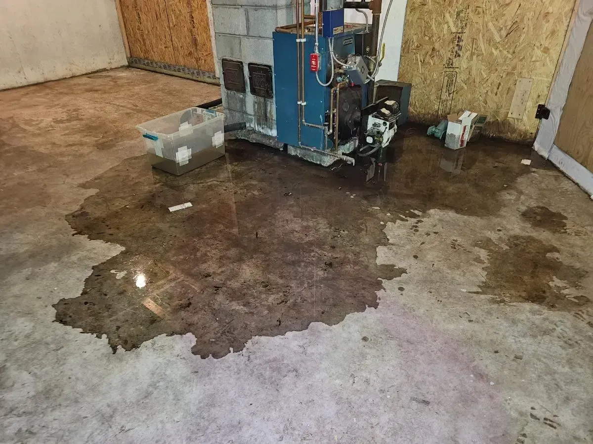 Flooded concrete basement floor with dark water near a boiler and plywood walls.