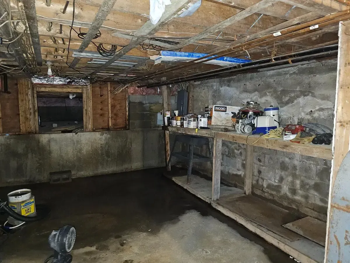 Basement workspace with concrete walls, workbench, and exposed ceiling beams.