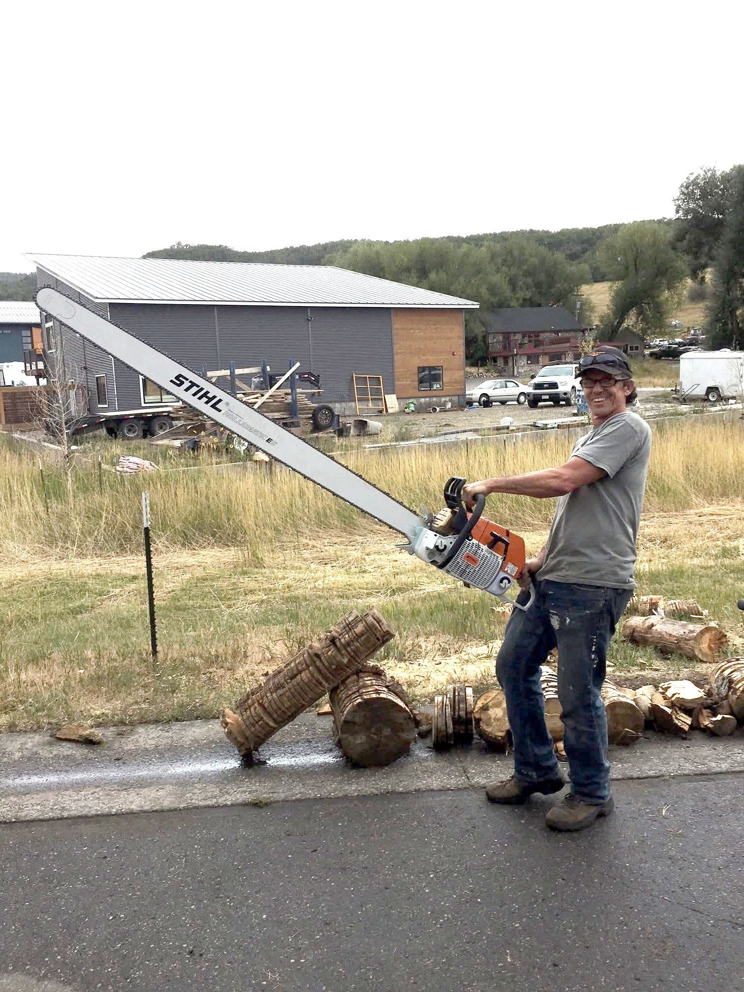 A man is standing on the side of the road holding a large chainsaw.